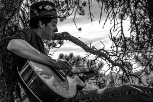 Quinlan Valdez by a tree with his guitar