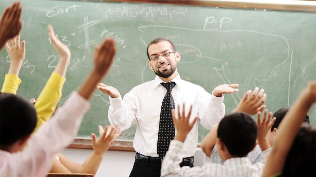 A professor making a question in a classroom and all the students are raising their hands to answer