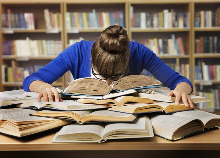 girl putting her head down in pile of books due to exam stress while studying