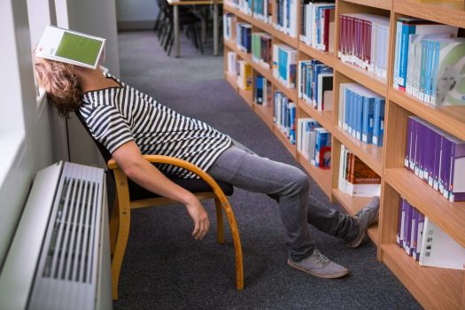 Student asleep in the library with book on his face at the university