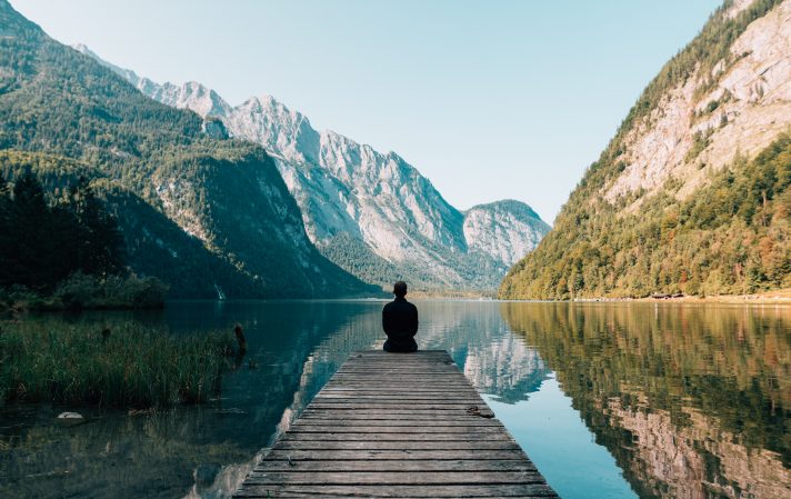 Person sitting at the edge of a dock in a valley showcasing this is what you can do if you get the easiest job to get and teach English abroad