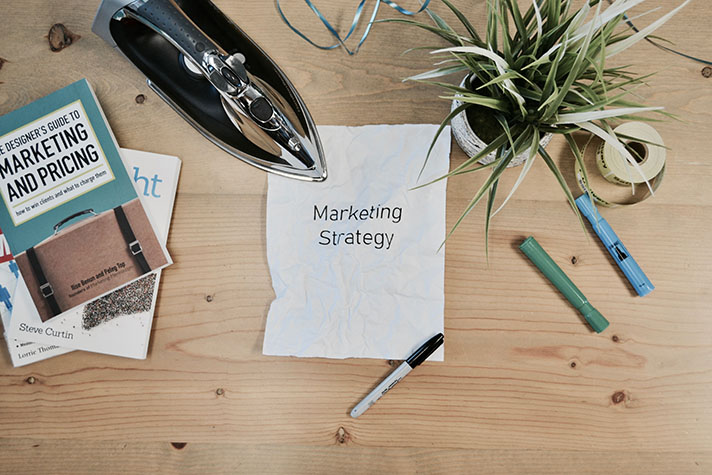 Photo of a desk with various desk ornaments and a sheet of paper with the writing marketing strategy in the center