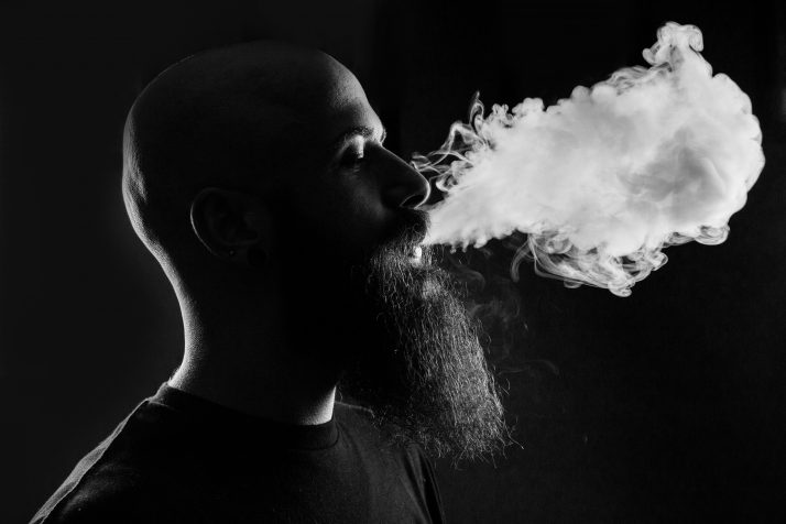 black and white image of a bearded man exhaling smoke