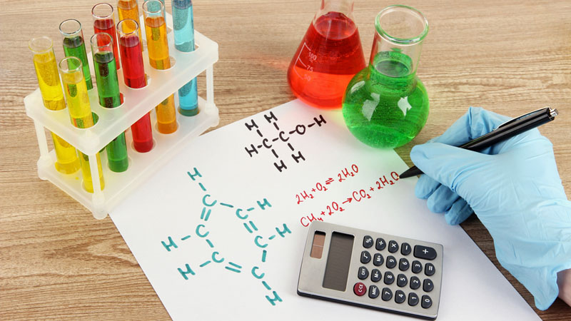 Test-tubes, conical flasks, a calculator, and a person's hand writing on a paper.