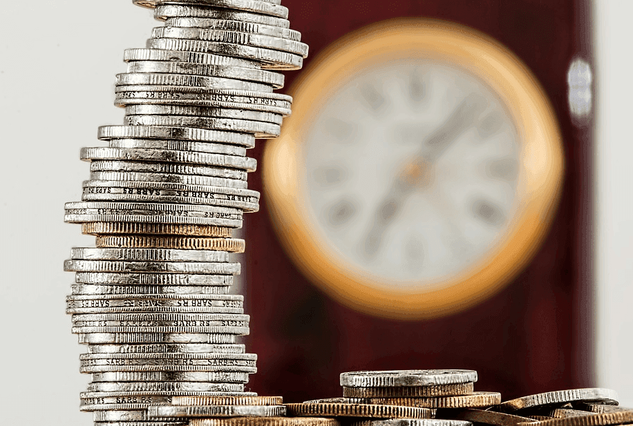 a stack of silver coins with a clock on the background