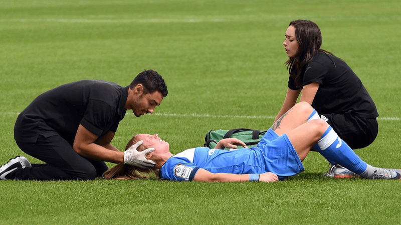 Two first aid personnel attending to a female athleteon a soccer field