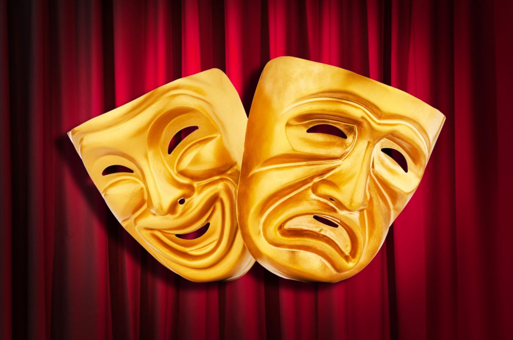 Two acting masks in front of a theatre curtain