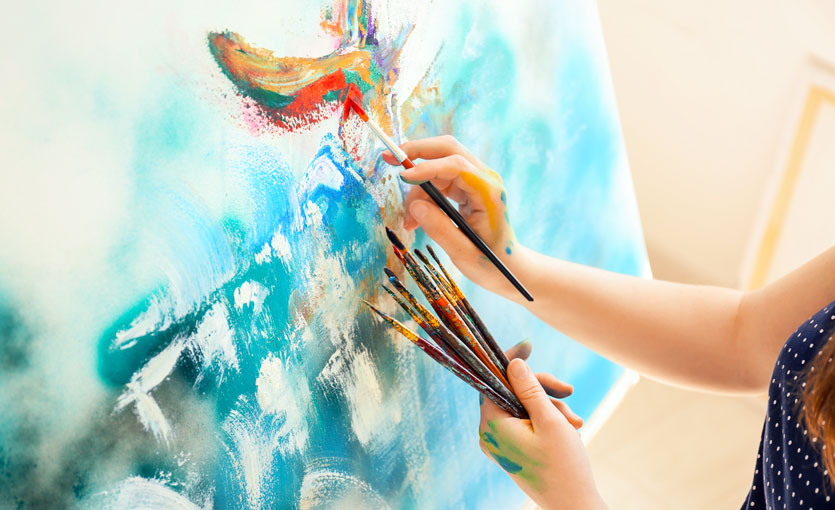 A painter holding brushes in one hand while painting with the other