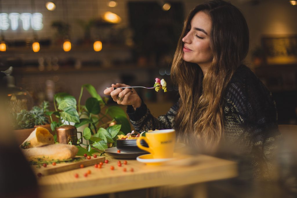 female student sitting down eating healthy food at a restaurant near purdue while smiling