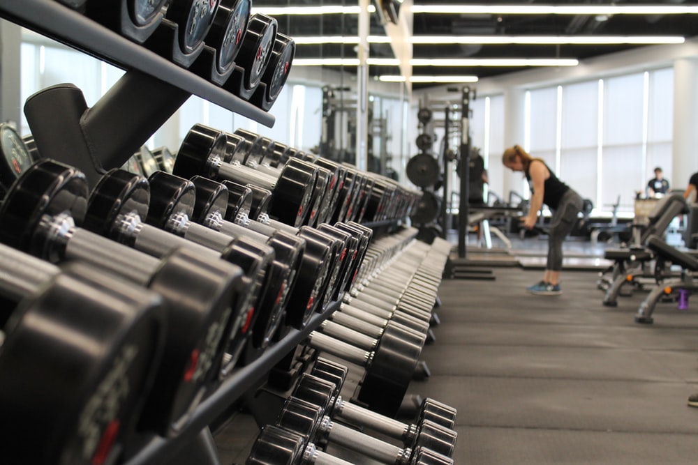 female student working out in campus gym with lots of weights around her