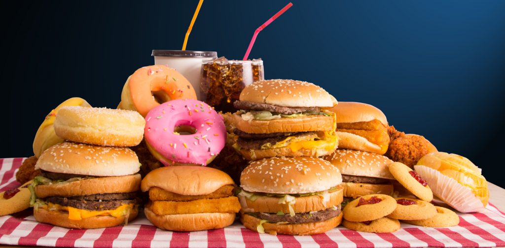 pile of burgers, donuts, milkshakes, fried chicken, etc. on a table