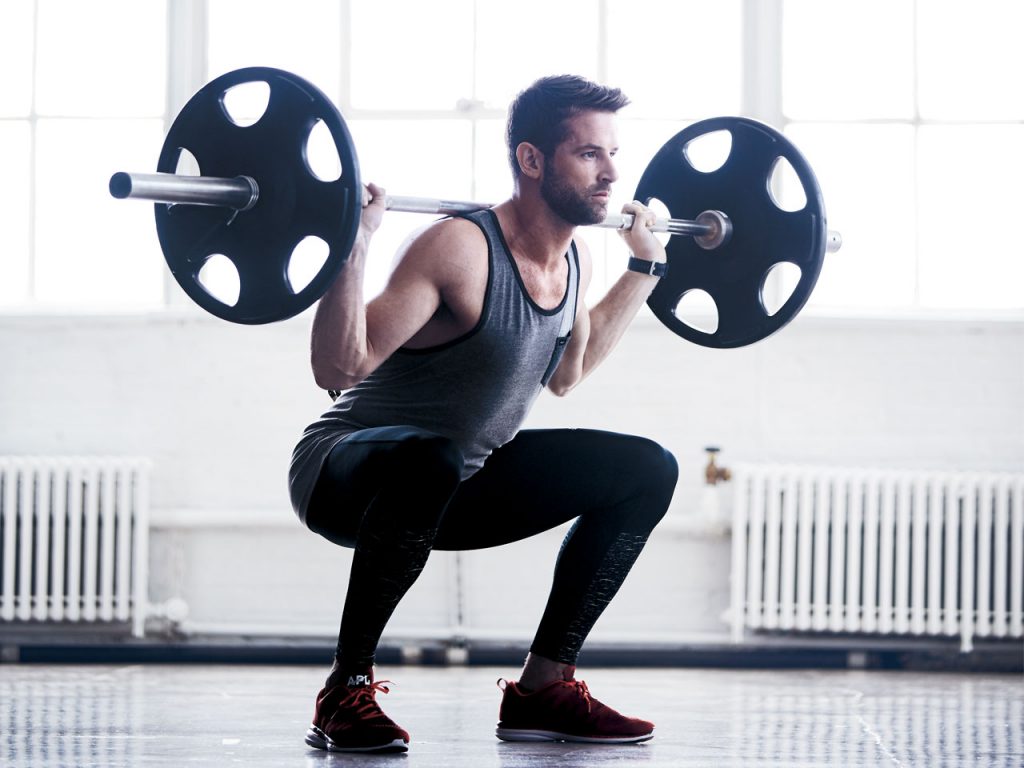 A man squatting with weights over his shoulder