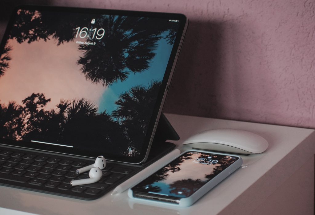technology products such as ipad with airpods and iphone on a desk, alongside an apple pen.