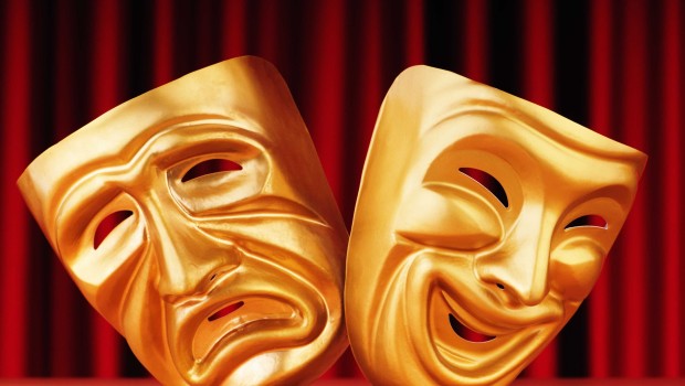 Two golden acting masks in front of a maroon curtain