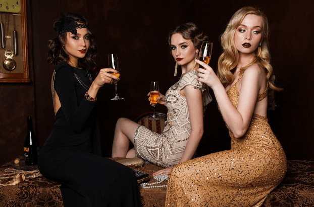 three ladies wearing beautiful dresses while drinking wine