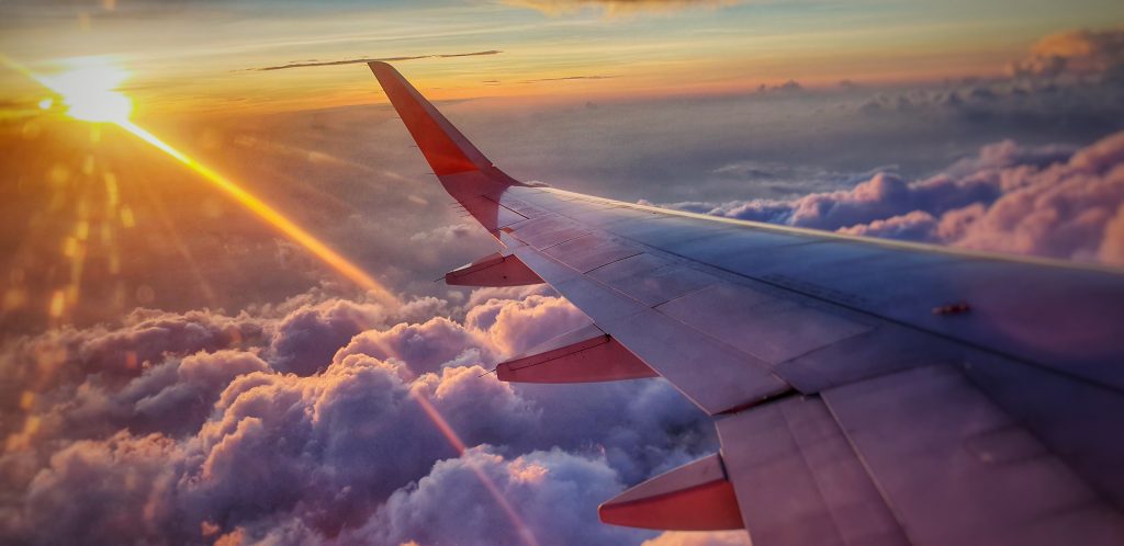 view of an airplane wing from a window seat high above the clouds with the sun setting