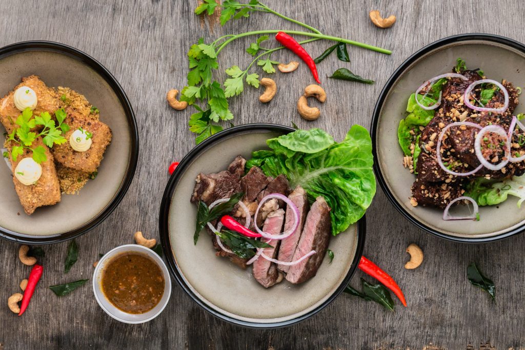 bowls of healthy foods such as quinoa, greens, and steak on a wooden table