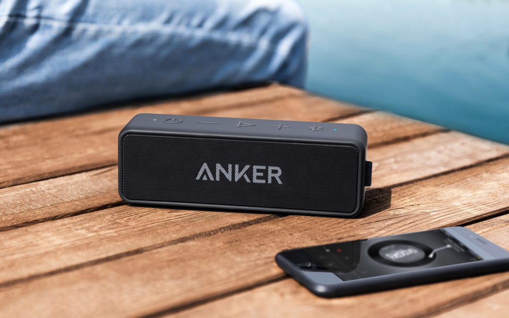 anker speaker next to an iphone playing music on a dock in the summer