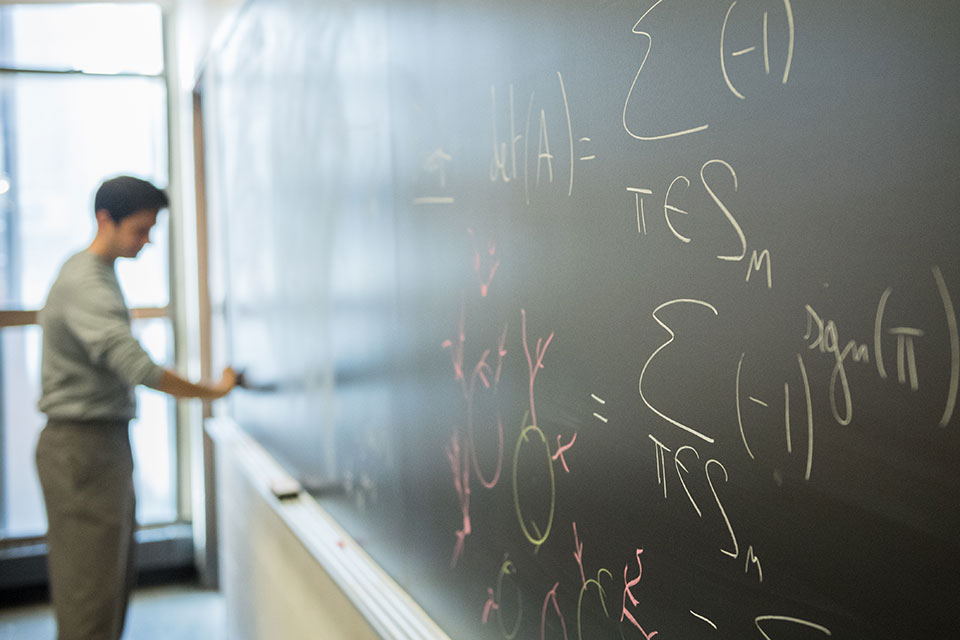 A math course instructor writing on a blackboard