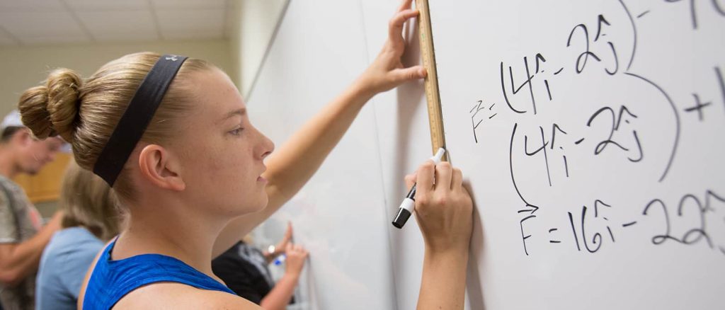 A math student at Texas A&M solving a mathematics problem on a white board .