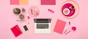 A pink desk with a laptop and office supplies laying around. 