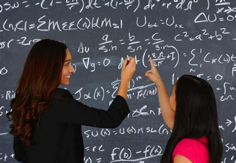 Two women writing solving math problems on the chalkboard. 